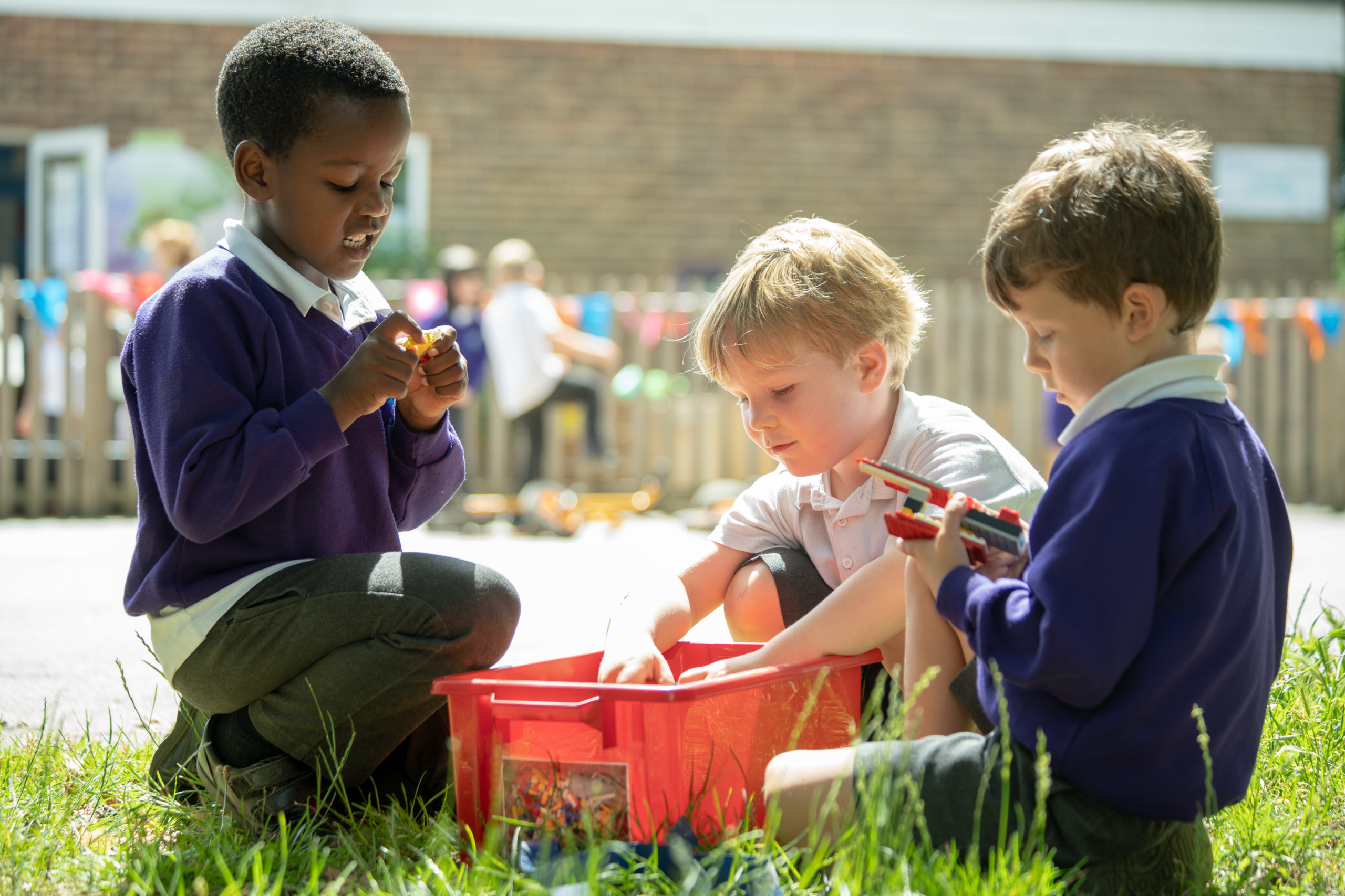 Three young pupils are shown playing together with a box of Lego on the school playground.