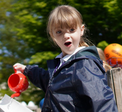 A child holding a watering can with an excited expression on her face